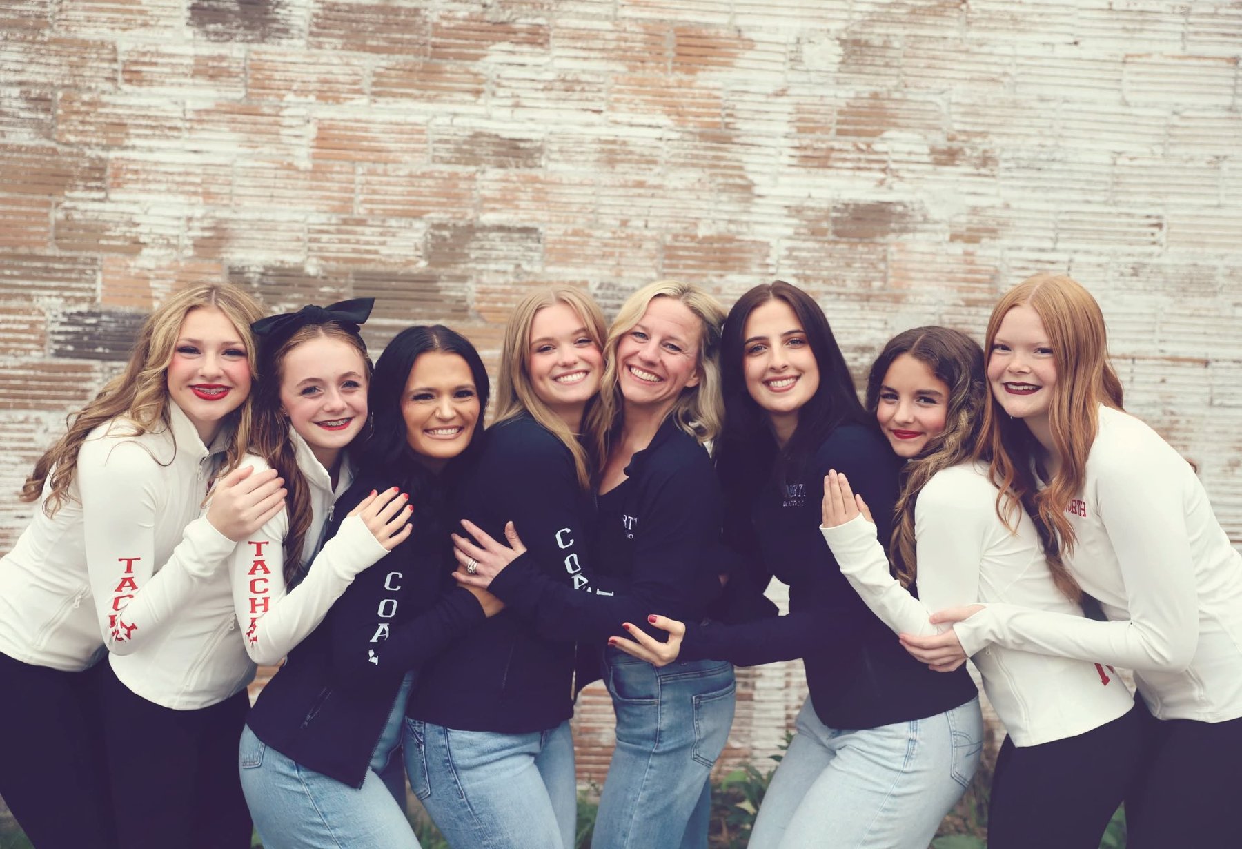 North Dance Studio dancers and coaches hugging together against a brick wall