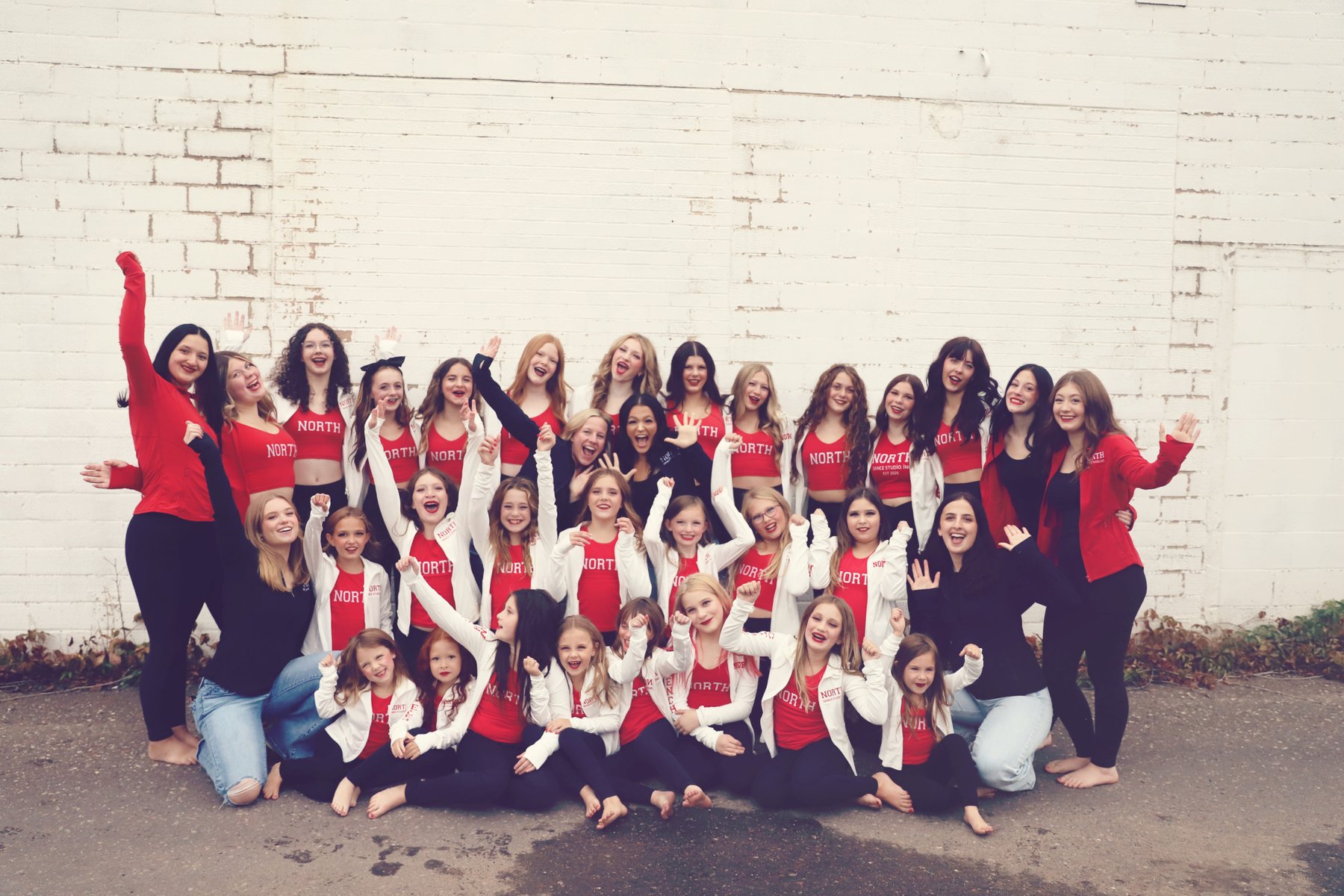 North Dance Studio dancers cheering together against a white brick wall