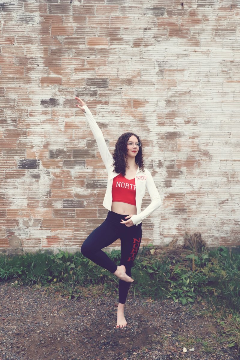 A North Dance Studio dancer balancing on one leg in front of a brick wall
