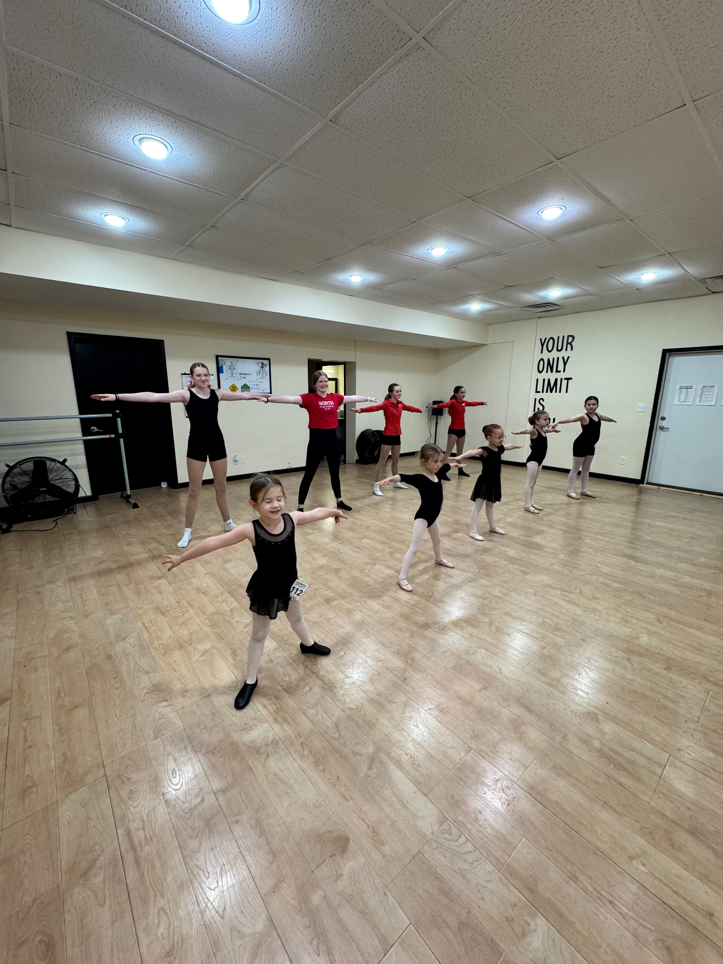 Dancers of all ages in ballet class with arms extended in second position