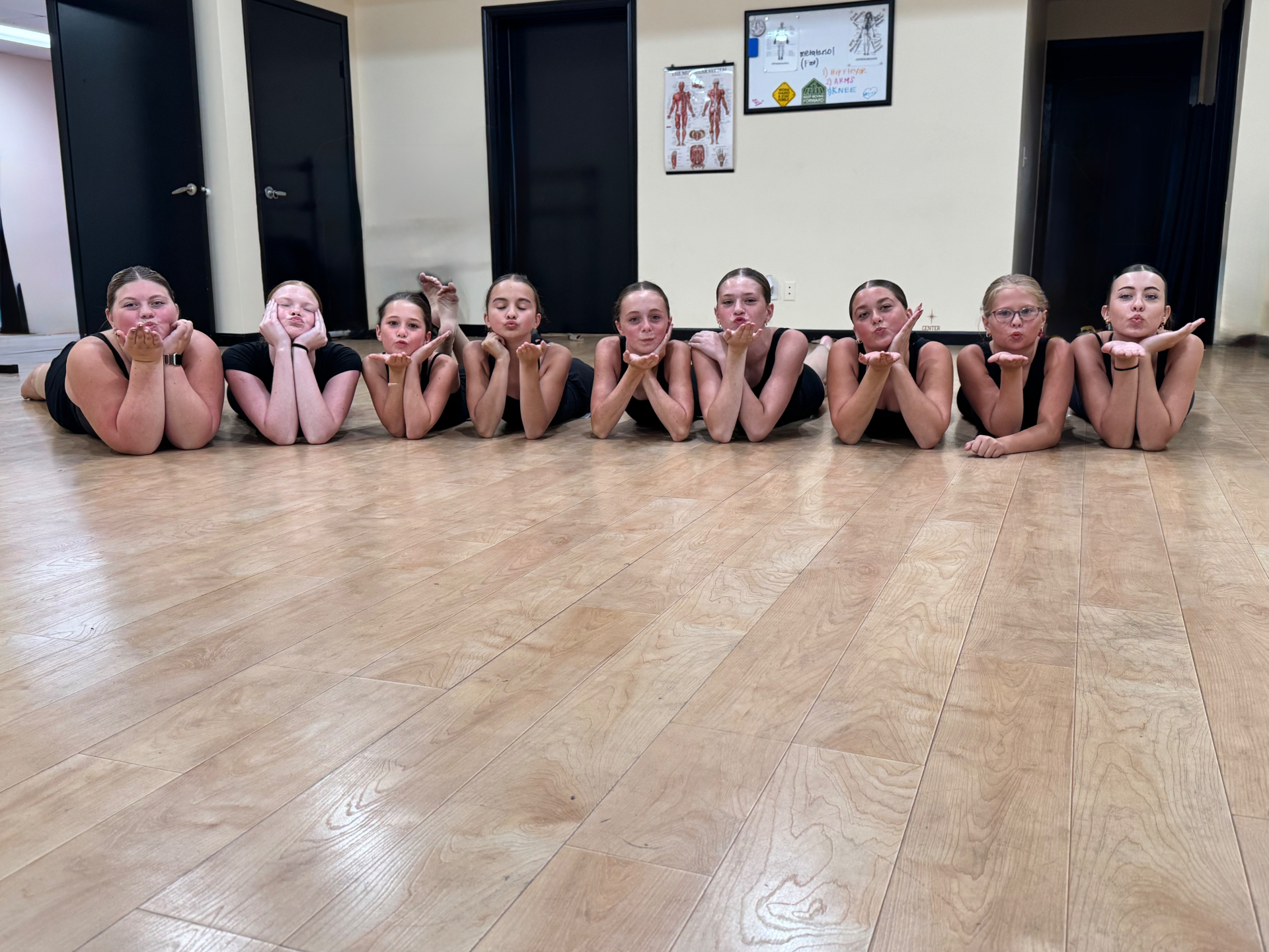Dancers lying in a line on the studio floor blowing kisses